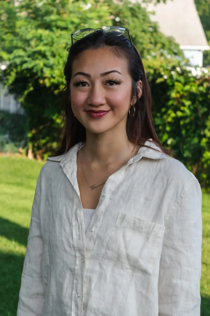 A woman in white shirt standing next to green grass.