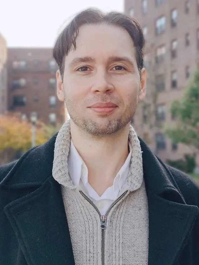 A man in a sweater and jacket standing outside.