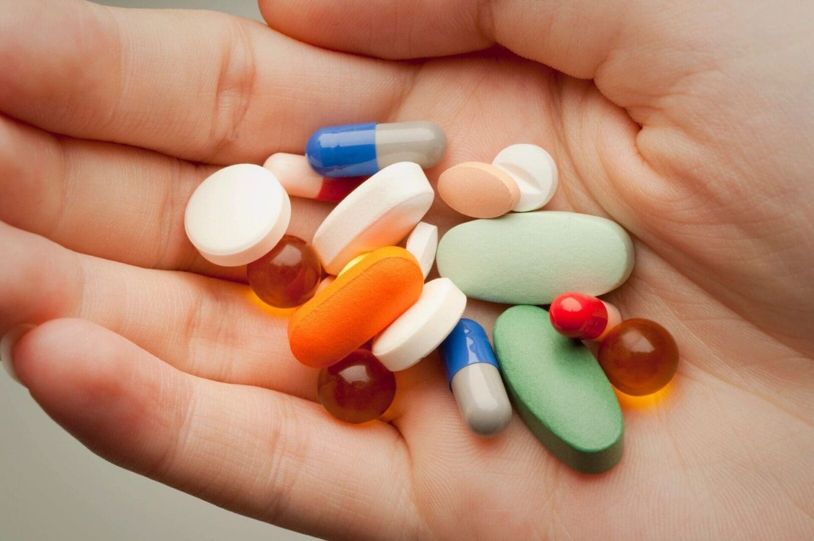 A person holding many different pills in their hand.