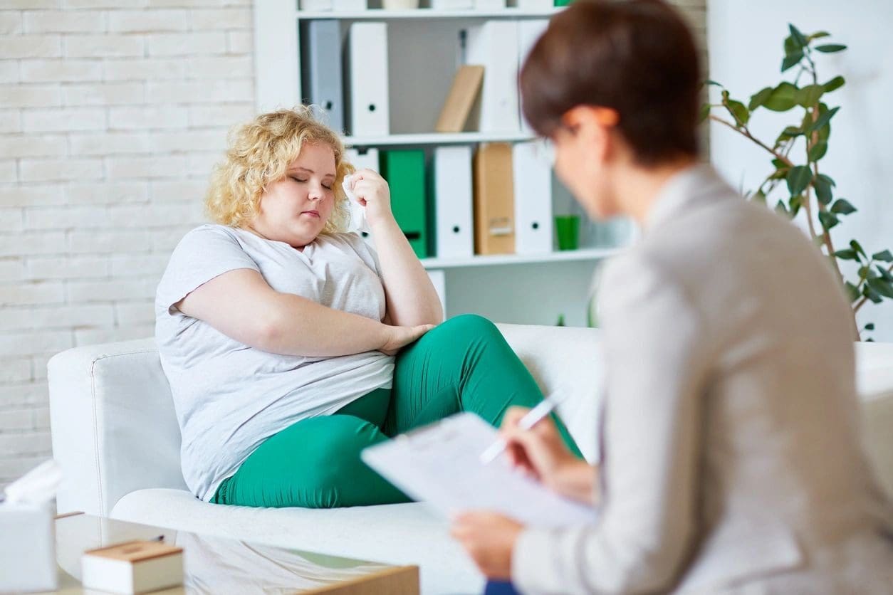 A woman sitting on the couch talking to another person.