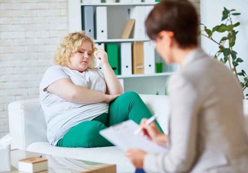 A woman sitting on the couch talking to another person.